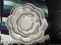 Top-down view of five stacked flower-shaped metal cake pans showing varying sizes and scalloped petal edges