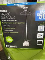 Front view of the Conair Ultimate Fabric Steamer box showing main product features, wattage, heat-up time, rotating hanger, hose, clips, and bonus kit.