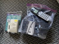 Four cordless phone handsets inside a plastic bag with charging bases, placed next to a new doorbell chime unit in original packaging on a carpeted floor.