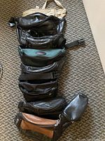 Eight assorted waist packs arranged vertically on a carpeted floor showing a variety of leather and fabric materials and colors such as beige, black, brown, and green.