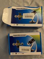 Two boxed USB digital microscopes in blue and white packaging labeled 'Digital Microscope'.