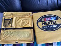 Yellow stadium cushion with NASCAR Nextel Cup Series logo, showing multiple zippered and mesh storage compartments for convenience during stadium events.
