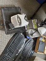 Image showing two black wireless keyboards, a white desk lamp, multiple black plastic file trays stacked, a white handheld Dymo label maker, and boxed Fios N300 modem and router, with some batteries scattered.