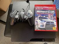 Top view of PS3 console with wired controller and Midnight Club Los Angeles Complete Edition game case on top.