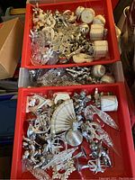 Three bins filled with many silver-colored Christmas ornaments showing variety in shapes and designs including angels, drums, and decorative foliage.