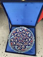 Top view of the hand-painted round plate inside the blue velvet presentation box, showing detailed floral and vine design.