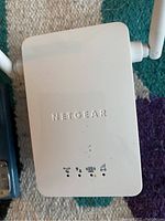 Close-up photo of white Netgear WiFi booster showing dual antennas and front indicator lights.