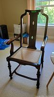 Full view of antique dark wood framed chair with cane seat and gently curved armrests.