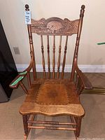 Full front view of antique wooden rocking chair with leather seat and carved backrest, showing overall wear and loose arm.
