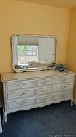 Full view of white wood dresser with attached large mirror above it showing overall style and condition.