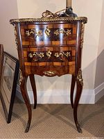 Full front view of the antique burled wood curio cabinet showing two drawers, top with brass edging, and brass feet.