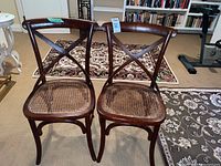 Two wooden chairs with cane seats and crossed backrests on carpeted floor.