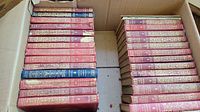 Top-down view of 27 hardcover books in red and blue cloth bindings with gold embossing, showing wear and usage marks.