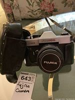 Fujica ST 801 SLR camera with attached lens and black leather case, sitting on glass table with strap visible.