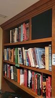 Full view of wooden bookshelf filled with approximately 30 hardcover books across three shelves of different topics including history and theology.