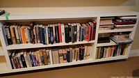 Wide view of two shelves of books, mostly hardcover with a diverse collection of titles in different colors and sizes.