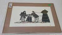 Framed limited edition Inuit stonecut print showing two Inuit figures pulling ropes and a third figure in the background, framed under glass with mat board.