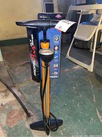 Full bike pump with black handle, black base, orange and silver body, and hose with gauge.