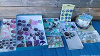 Overview of multiple containers filled with beads by color and type arranged on a table, including trays and small compartments.