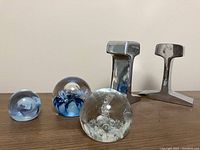 Three blown glass paperweights and two metal bookends displayed against a plain background, showing size and appearance.