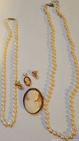 Photo of two pearl necklaces displayed alongside a cameo brooch, cameo pendant, and matching cameo earrings.