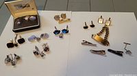 Overall lot showing 7 sets of men's cuff links and several tie clips with a range of designs and colors, including a boxed satin-lined set.