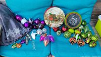 Wide view showing assortment of glass ornaments in vibrant colors, two Christmas tins, and fabric skirt.