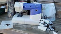 Huskystar 224 sewing machine with user guide, foot pedal, and fabric carry bag visible, set on wooden surface.