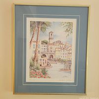 Framed watercolor print by Michele Gallego depicting a scenic view of Cannes with palm trees and buildings, with blue matting and a beige frame.