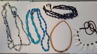 Six vintage necklaces laid flat showing different styles and bead colors including blues and whites.