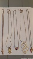 Full view of five silver-toned necklaces laid flat showing their chains and various pendants including ankh cross, owl, heart, interlocking rings, and pointed shapes.