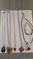 Full view of 5 necklaces and 1 bracelet displayed on white background showing chain lengths and pendant styles.