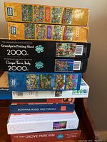 Stack of ten jigsaw puzzle boxes showing brand names, piece counts, and puzzle themes.