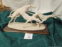 Front and side angle view of white bisque sculpture depicting three racing greyhounds mounted on a wood base, showing detailed anatomy and dynamic pose.