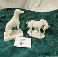 Photo showing both the female greyhound and white horse ceramic figurines placed on a green cloth. The figurines are in good condition and clearly display their shapes and texture.