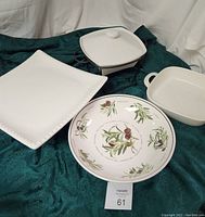 Photo showing all four ceramic serving pieces: square pedestal cake stand, square baker, olive print round bowl, and 2-quart baker with metal stand and lid