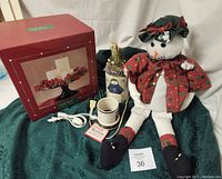 Photo of plush snowman in festive red scarf and black hat beside candle garden and votive warmer on green cloth.