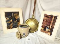 Photo of two signed and numbered photographs, a vintage brass bed warmer, and a stoneware crock with lid.
