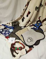 Group photo showing the fleece throw with dog motif as background, placement of metal bookend, two pet placemats, dog bandana, dog harness, and blue leash.