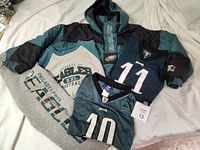 Wide view of the full lot laid on a light surface: hooded jacket, sweatpants, jerseys, and Gridiron Classic shirt.