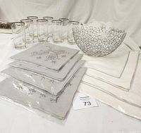Full view of the Napkins, Glasses, and Wire Decorative Basket arranged together showing the grey embroidered napkins in packaging, ivory napkins, glasses, and flower motif wire basket.