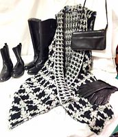 Lot laid out showing two pairs of black leather boots, a black white and gray long-knit vest, black leather cross-body purse, and black leather gloves on the vest.