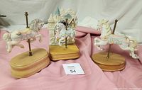 Three vintage ceramic carousel horse music boxes on wooden bases displayed with pink fabric background