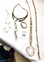 Photo of seven jewelry pieces displayed on a white surface: four necklaces including one large clear pendant, black and gold choker, white bead necklace, and slim gold-tone chains; two watches, one silver Anne Klein and one gold Pulsar; and one gold-tone textured ring.