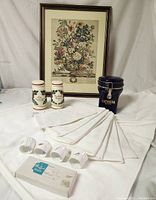 Full lot featuring framed botanical print, tablecloth with napkins, pottery shakers, coffee canister, and napkin rings arranged on a white cloth background.