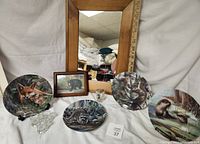 Full lot photo showing the four Edwin Knowles collector plates with animal designs, three small clear handled shot glasses, a framed black bear picture, and a wood framed mirror.