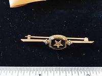 Front view of the 10 Kt gold Mason bar pin showing the onyx-colored central stone with a Masonic star symbol and two seed pearls on either side, on a black background with a ruler for scale.