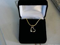 Gold heart-shaped pendant on chain displayed inside a black velvet box with white satin interior.