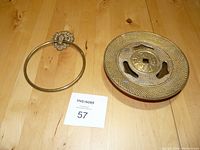 Photo showing both brass items, the lion head towel holder ring and the incense burner with removable lid, on a wood surface.