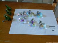 Photo showing 6 crystal cut drawer knobs with silver screws and 3 solid green dinosaur drawer knobs arranged on a sheet of paper on a wood table